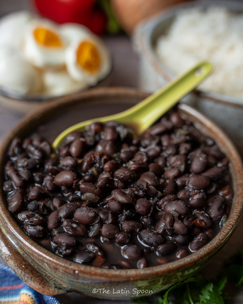 Medium-sized bowl filled with fully cooked black beans, with a green spoon scooping some out.