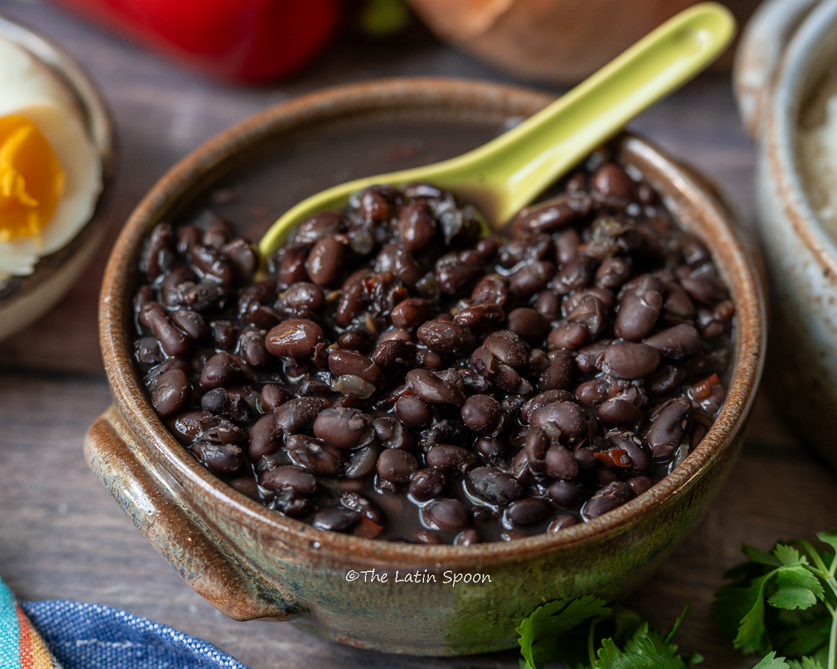 Medium-sized bowl filled with fully cooked black beans, with a green spoon scooping some out.