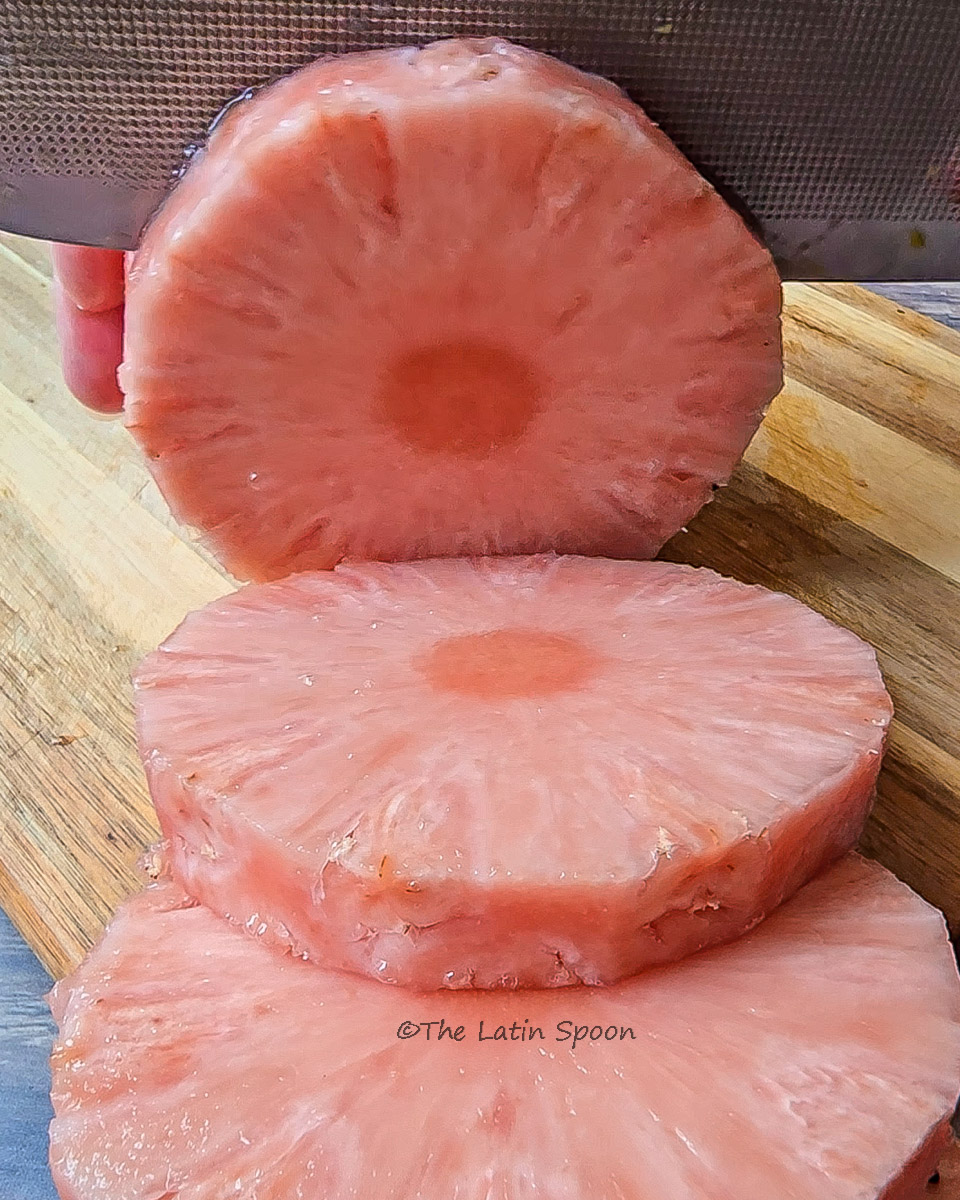 Peeled pink pineapple sliced into rounds on a wooden cutting board.