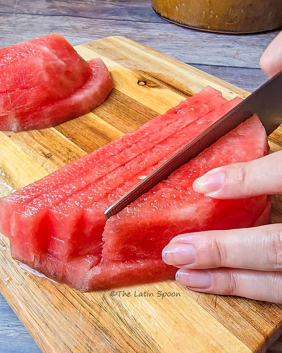 Watermelon being sliced into long strips on a wooden cutting board.