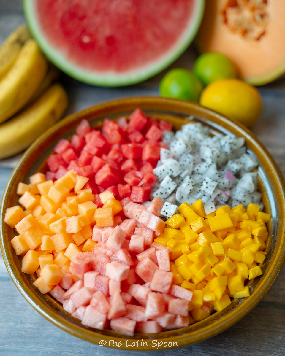 Bowl of tropical fruit salad with mango, pineapple, watermelon, and melon pieces arranged separately.