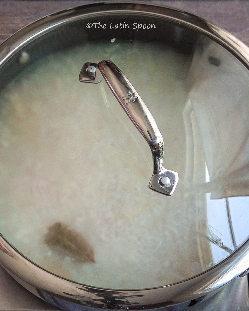 A clear glass lid showing rice cooking in water, with bay leaves floating on top