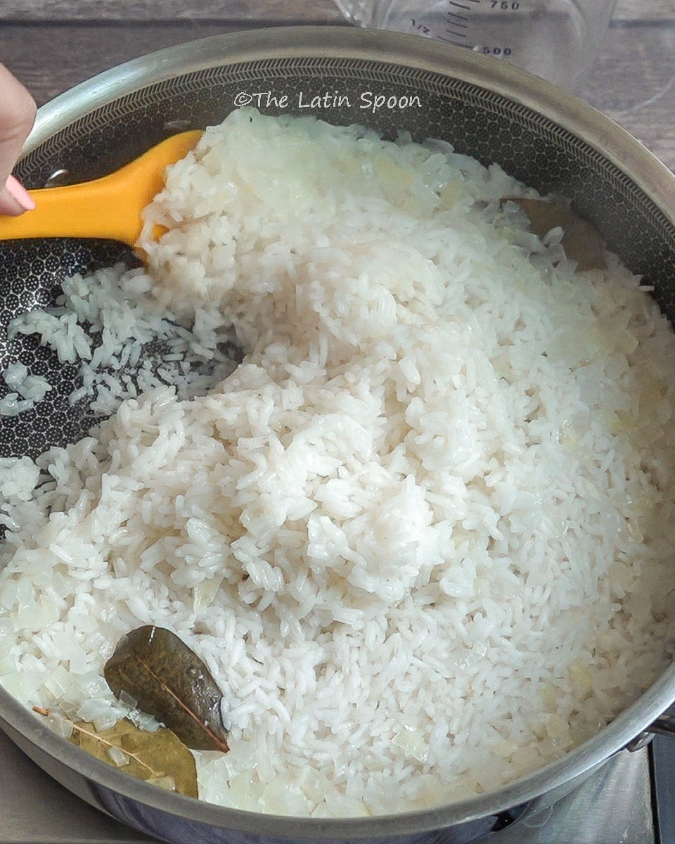 Stirring rice very gently with a spatula; bay leaves rest on top after being cooked on the stove