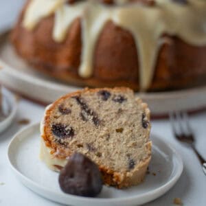 A close-up of a slice of fig cake with a caramelized fig from the preserves in front of it, while the rest of the cake is visible in the background.