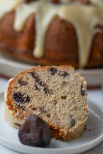 A close-up of a slice of fig cake with a caramelized fig from the preserves in front of it, while the rest of the cake is visible in the background.