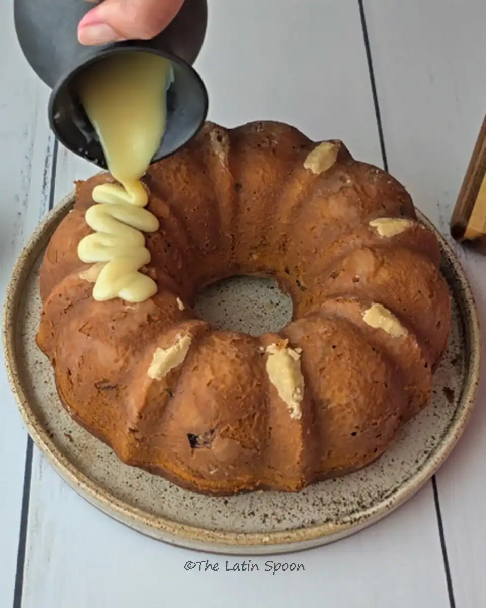 A baked bundt cake as condensed milk glaze is slowly poured on top, spreading across the surface.