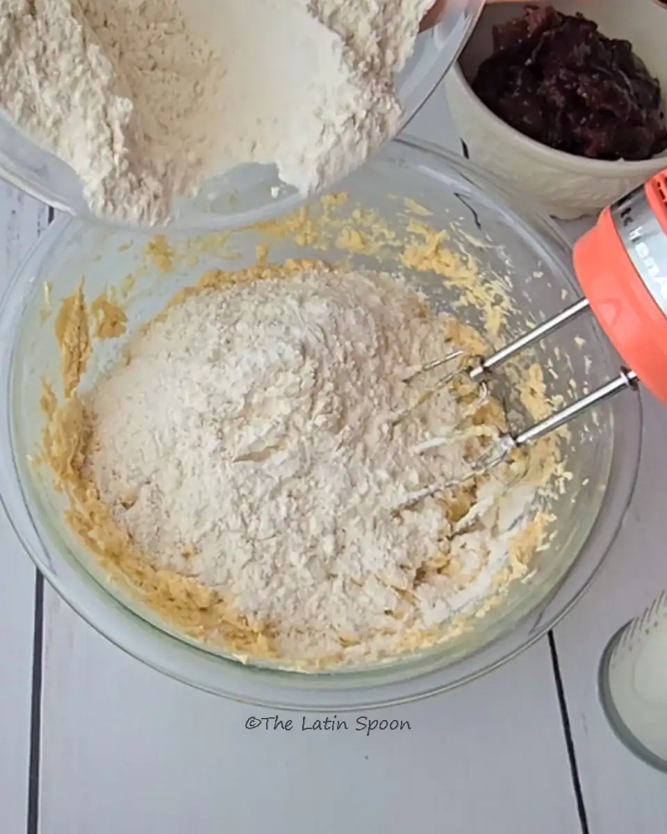 The cake-making process showing dry ingredients — flour, salt, and baking powder — being added to the butter mixture while the mixer is stopped.