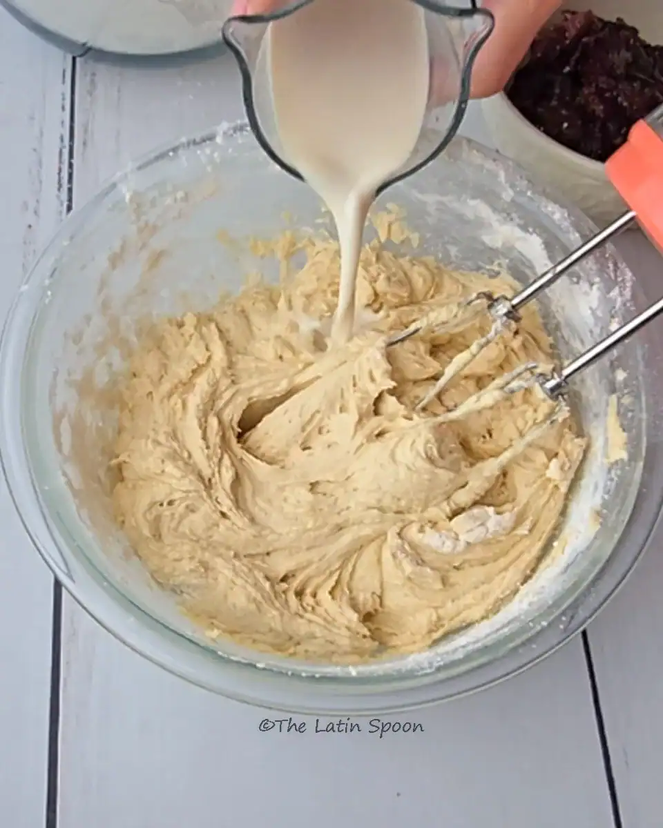 The cake batter preparation process showing milk being added slowly while the stand mixer is paused.