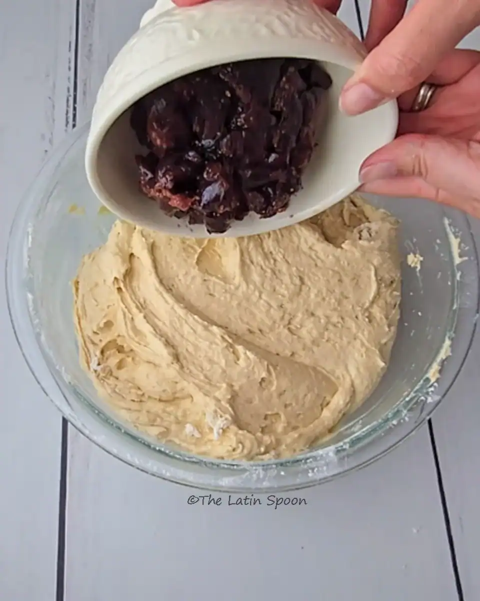 A glass bowl with the cake batter, and a second bowl adding diced figs into the mixture.