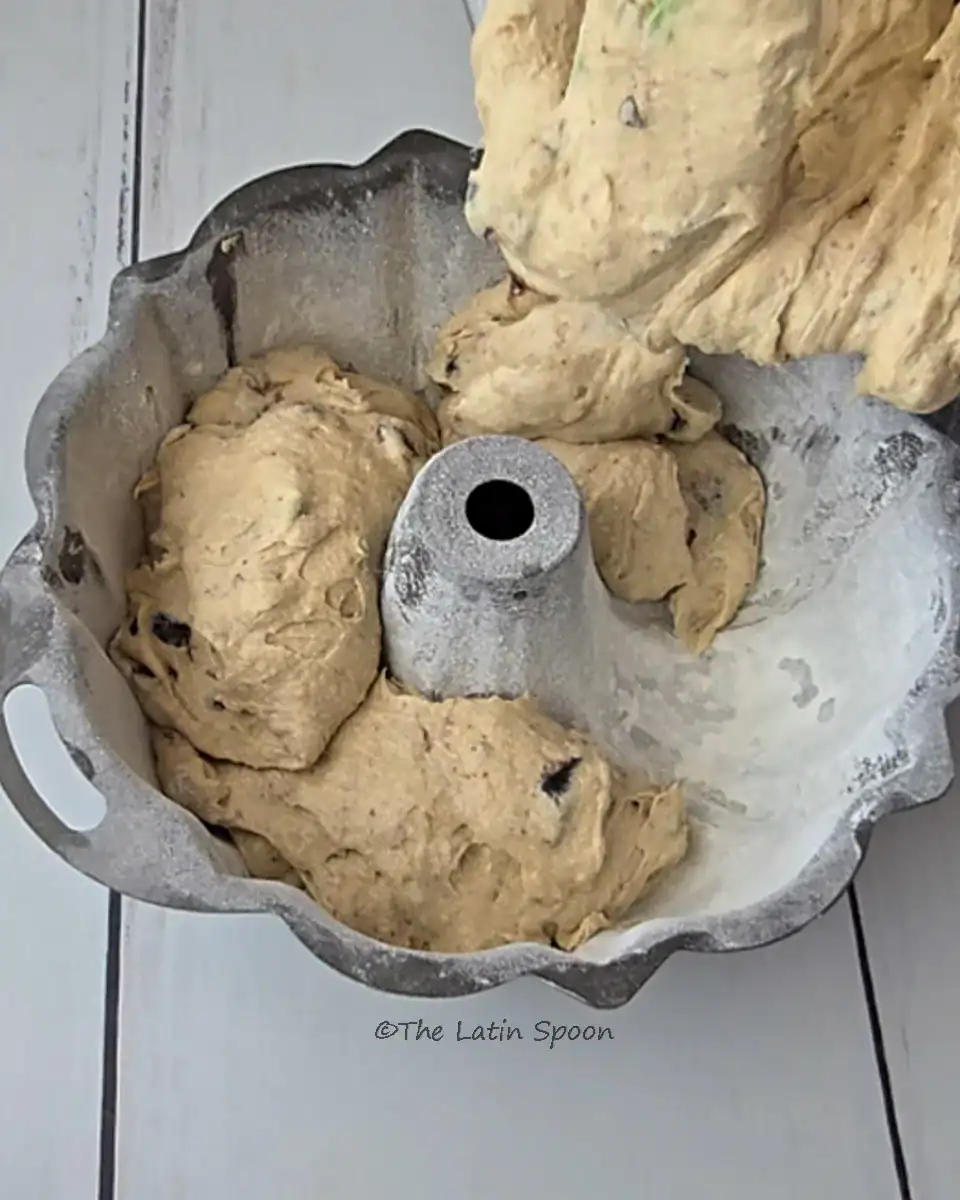 A prepared bundt cake pan, greased and floured, being filled with the fig cake batter, ready to be baked.