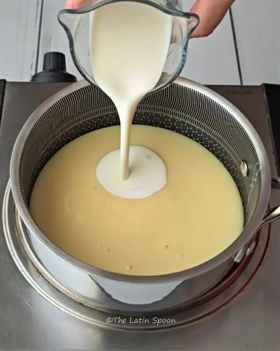 A small pot with condensed milk as heavy cream is slowly being added to the mixture