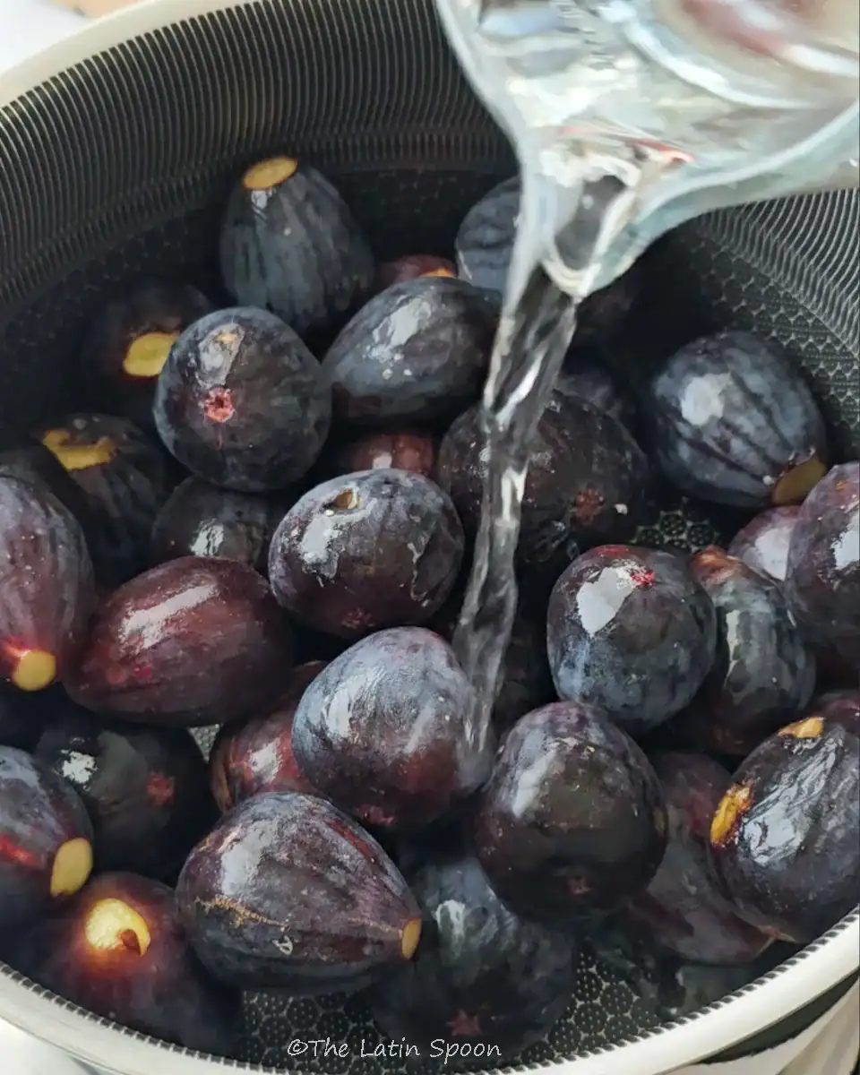 A pot filled with fresh figs while a pitcher pours water into it.
