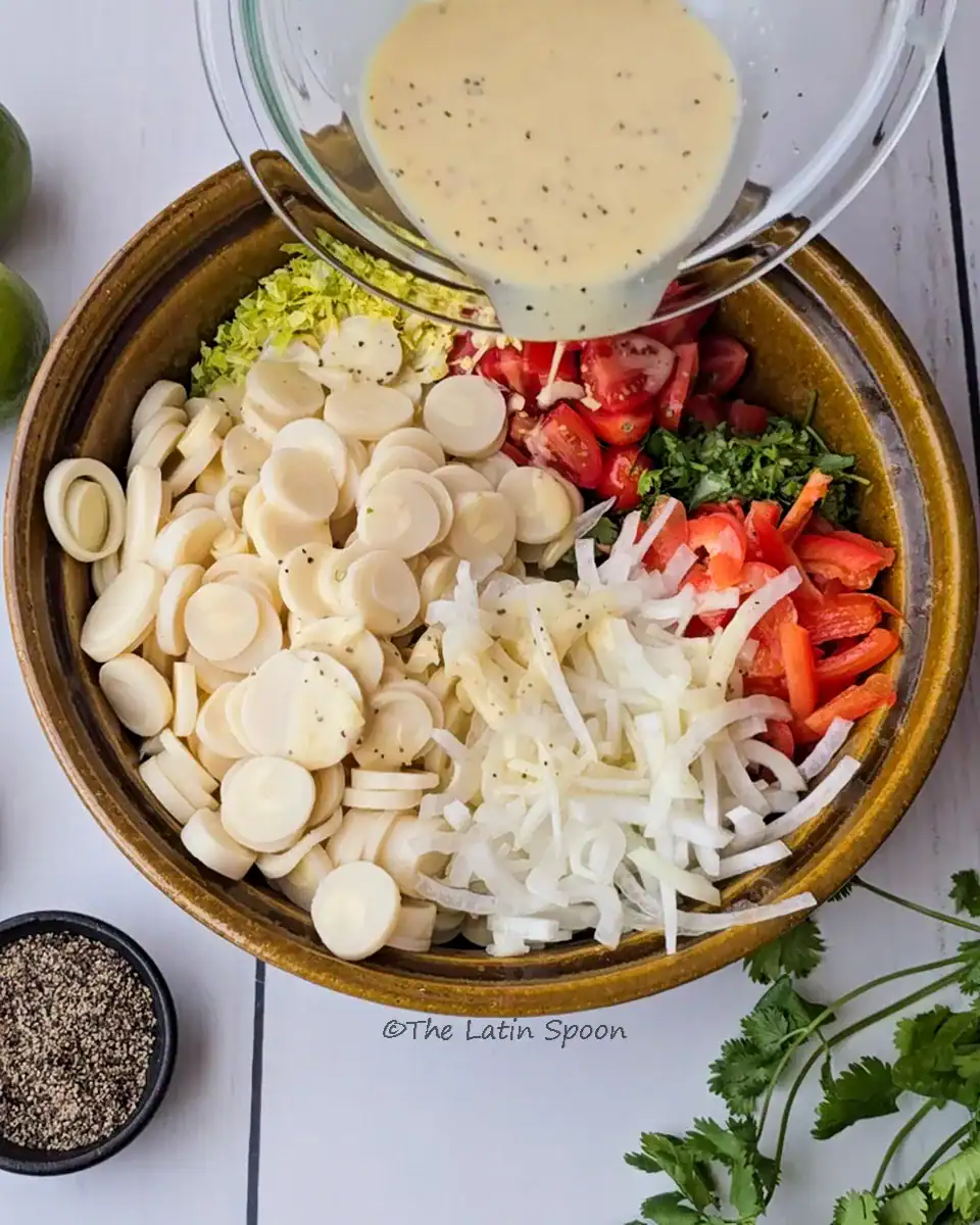 A brown bowl with all the salad ingredients separated — heart of palm on one side, onion, tomatoes, and other vegetables next to it — and a second bowl pouring dressing on top.