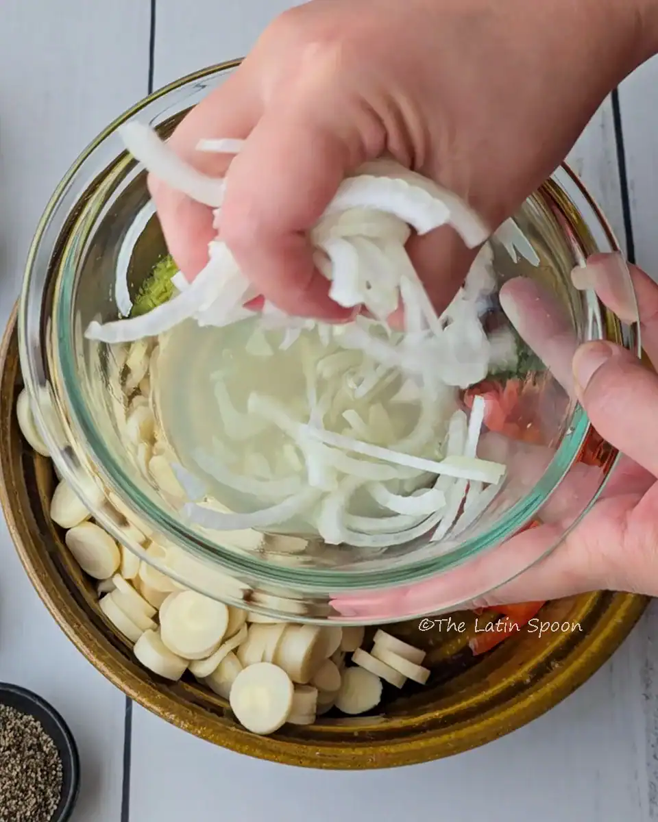 A brown bowl with the salad ingredients, while a left hand holds a second bowl above it, separating the onions from the lemon juice left in the bowl.