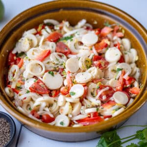 A brown bowl holding the heart of palm salad, showing pieces of heart of palm, tomato, red bell peppers and other ingredients.