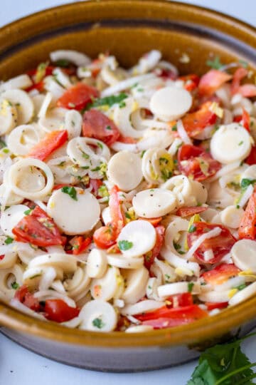 A brown bowl holding the heart of palm salad, showing pieces of heart of palm, tomato, red bell peppers and other ingredients.