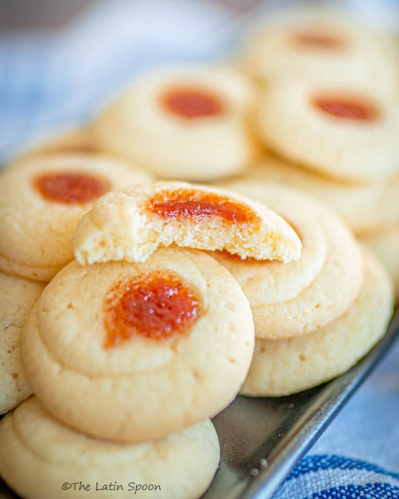 Round butter cookies topped with guava jam, one cookie cut in half to show the soft texture inside.