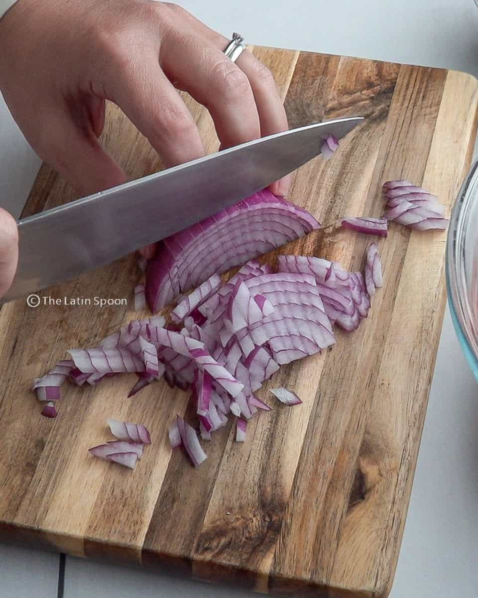 On a cutting board, a red onion is being chopped into small pieces with a knife.