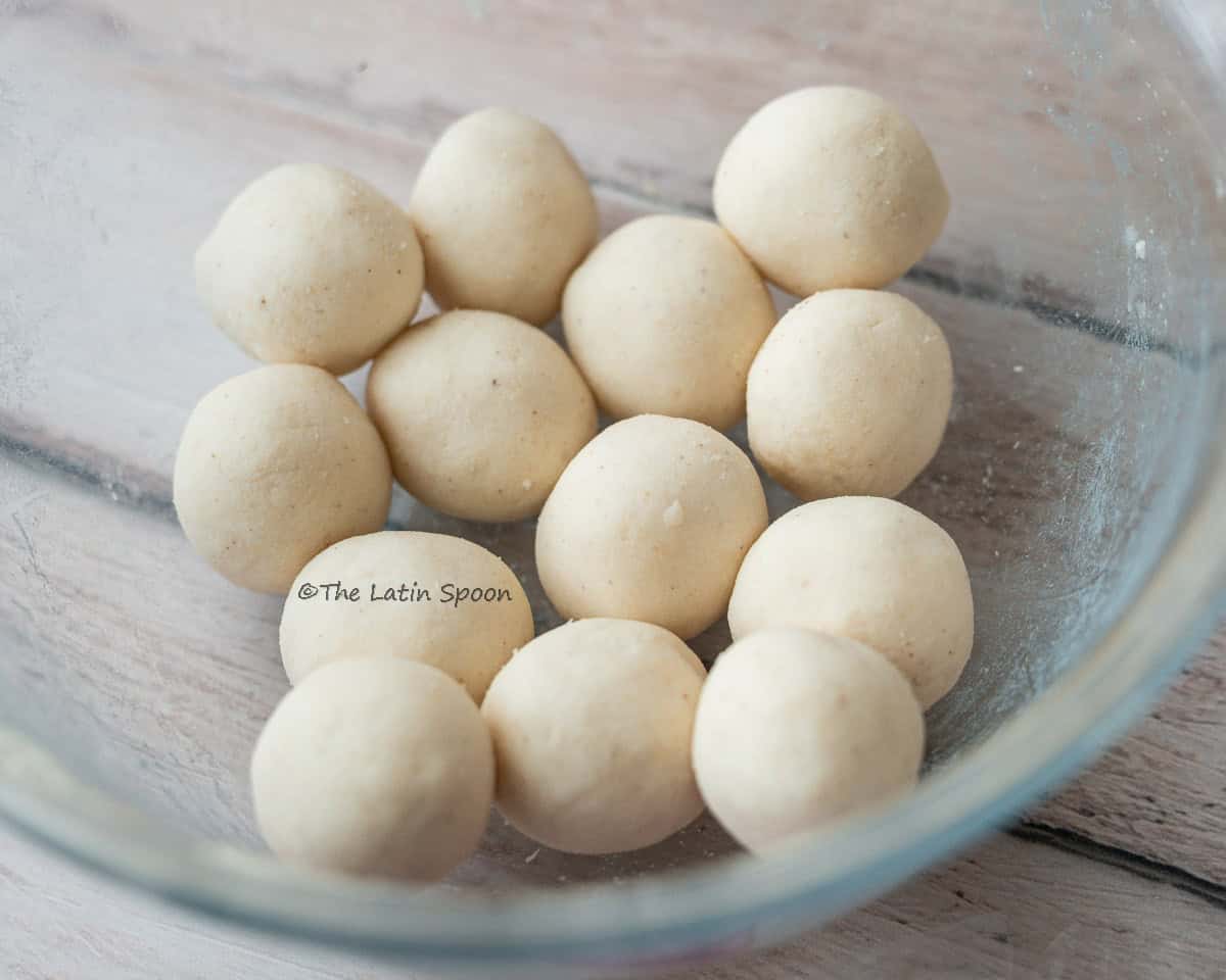 Small dough balls of similar size arranged inside a clear glass bowl.