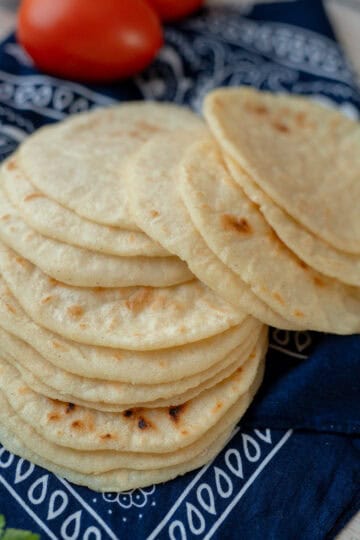 Freshly hand-shaped tortillas resting on a traditional Costa Rican cloth, with tomatoes in the background.