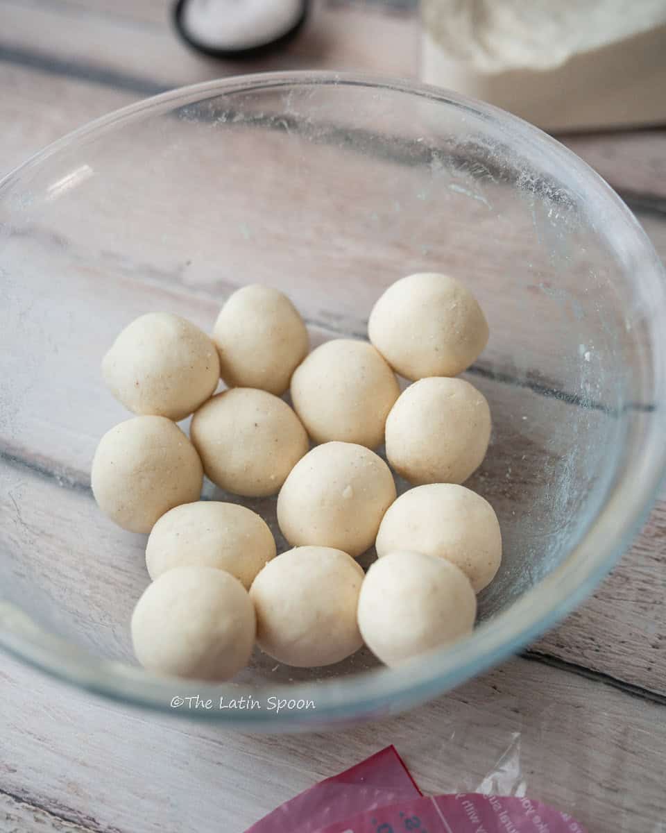 Small dough balls of similar size arranged inside a clear glass bowl.