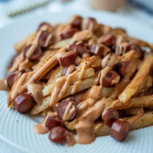A plate of French fries and sliced sausages topped with pink sauce.