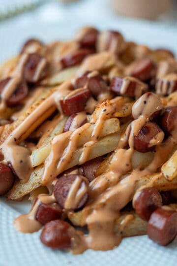 A plate of French fries and sliced sausages topped with pink sauce.