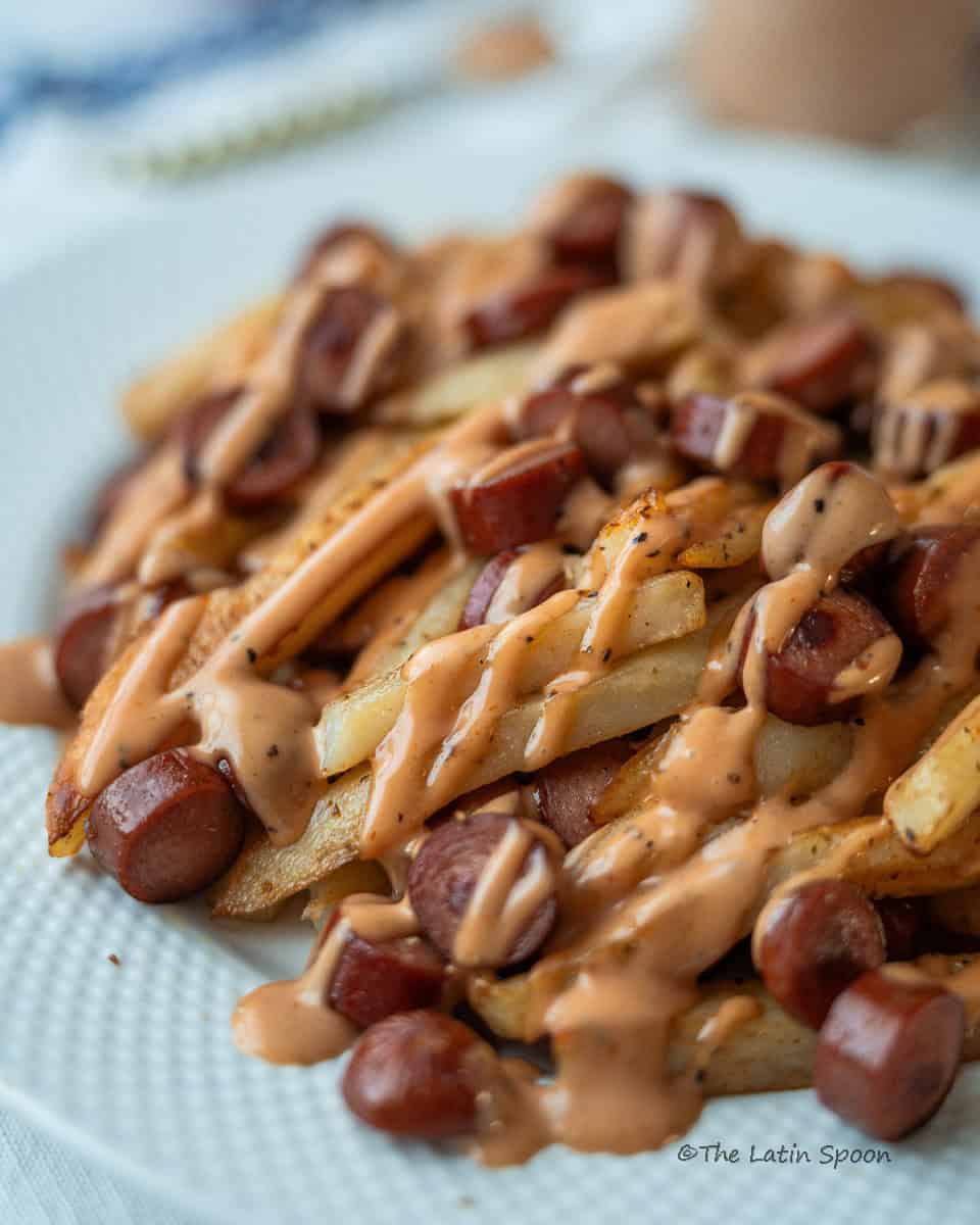 A plate of French fries and sliced sausages topped with pink sauce.