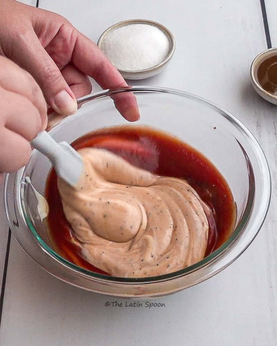 A bowl with all the ingredients mixed together, held by the left hand while the right hand stirs the mixture with a spatula.