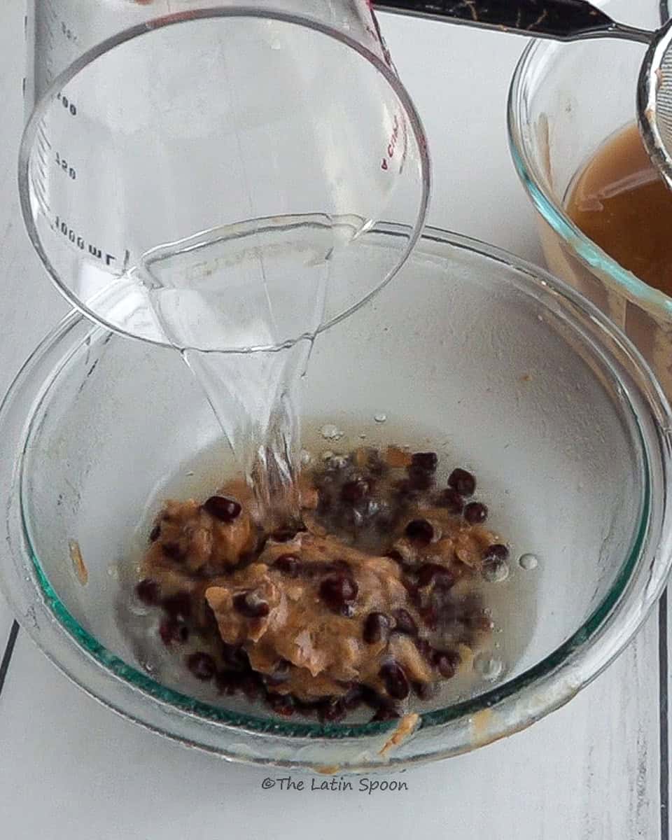 A pitcher tilted, pouring water into a bowl containing tamarind pulp and seeds left after straining.