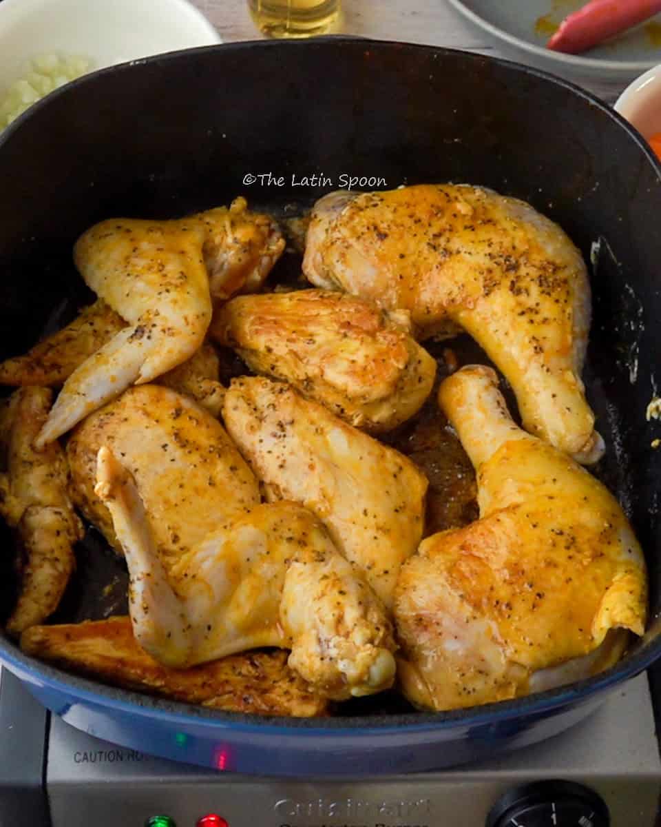 A Dutch oven with the chicken pieces cooking starting to turn golden