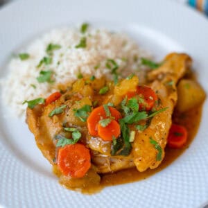 A plate with a piece of chicken and carrots, served with white rice and decorated with little pieces of fresh cilantro