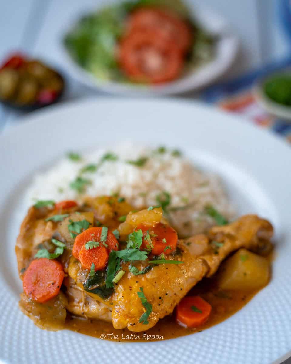 A serving plate with chicken, carrots, and potatoes, and in the background, slightly blurred, a bowl of salad.