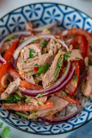 A round blue bowl showing the finished tuna salad with pieces of tomato and cilantro visible in the background.