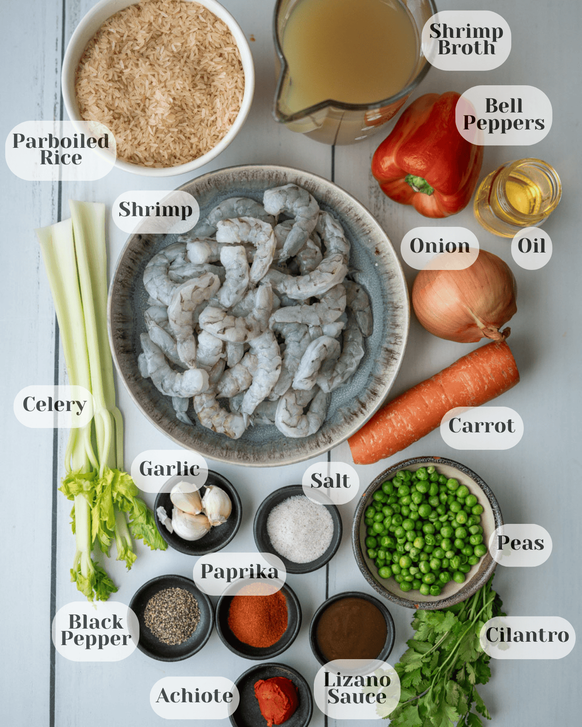 Ingredients for arroz con camarones including shrimp, rice, vegetables, spices, achiote, and shrimp stock laid out on a table.