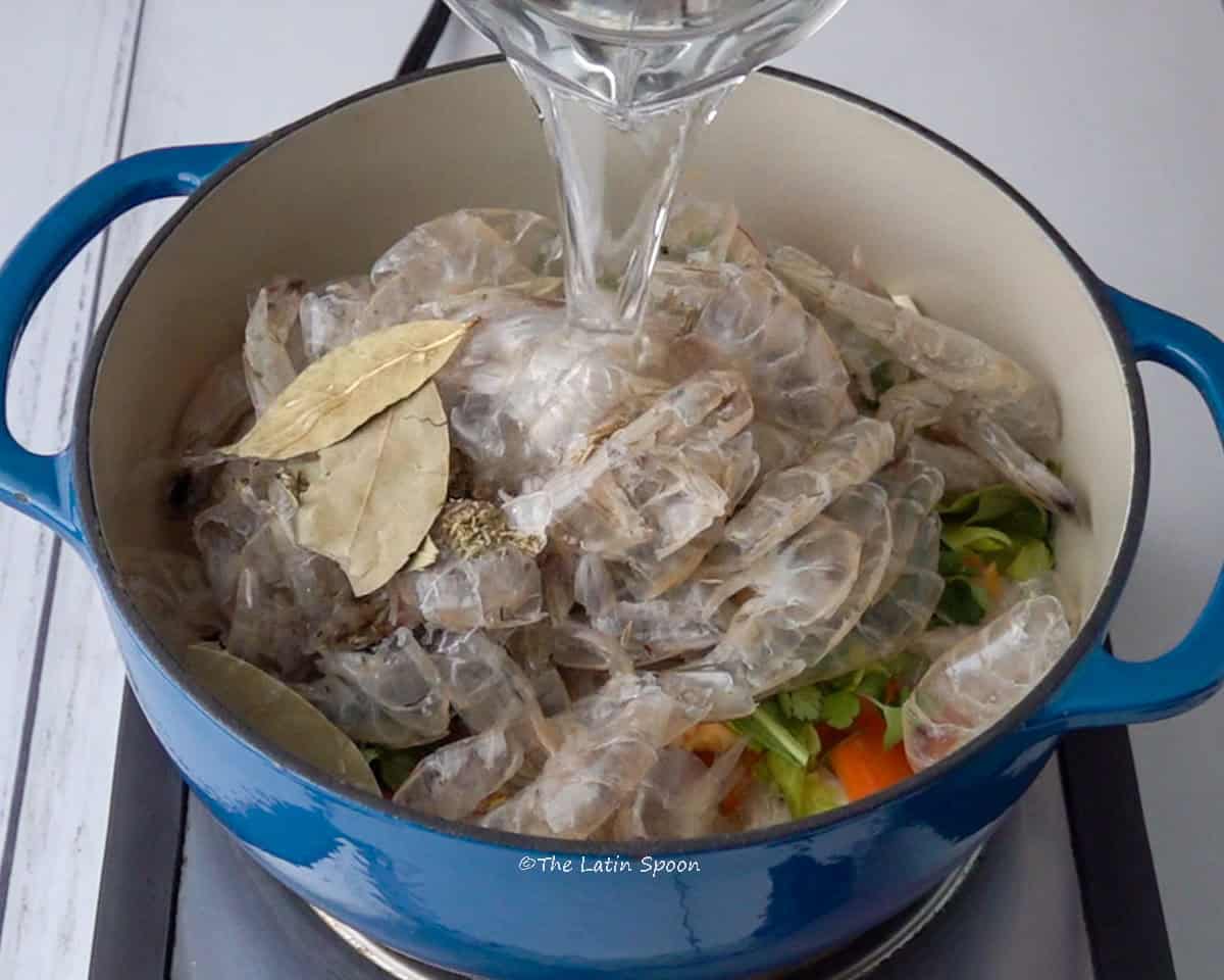 A pot with shrimp shells and vegetables while water is being added.