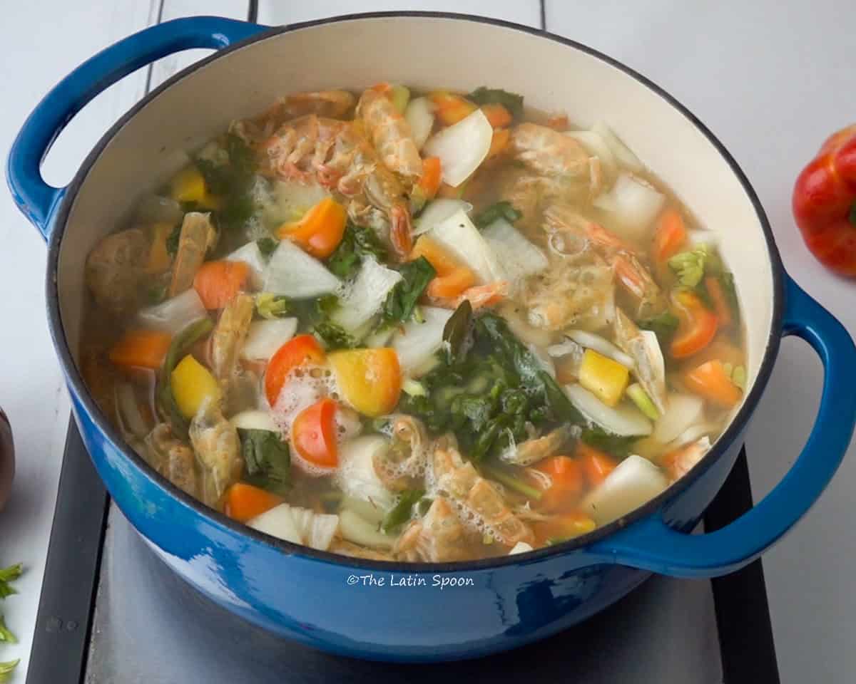A pot with vegetables, spices, and shrimp shells gently simmering.