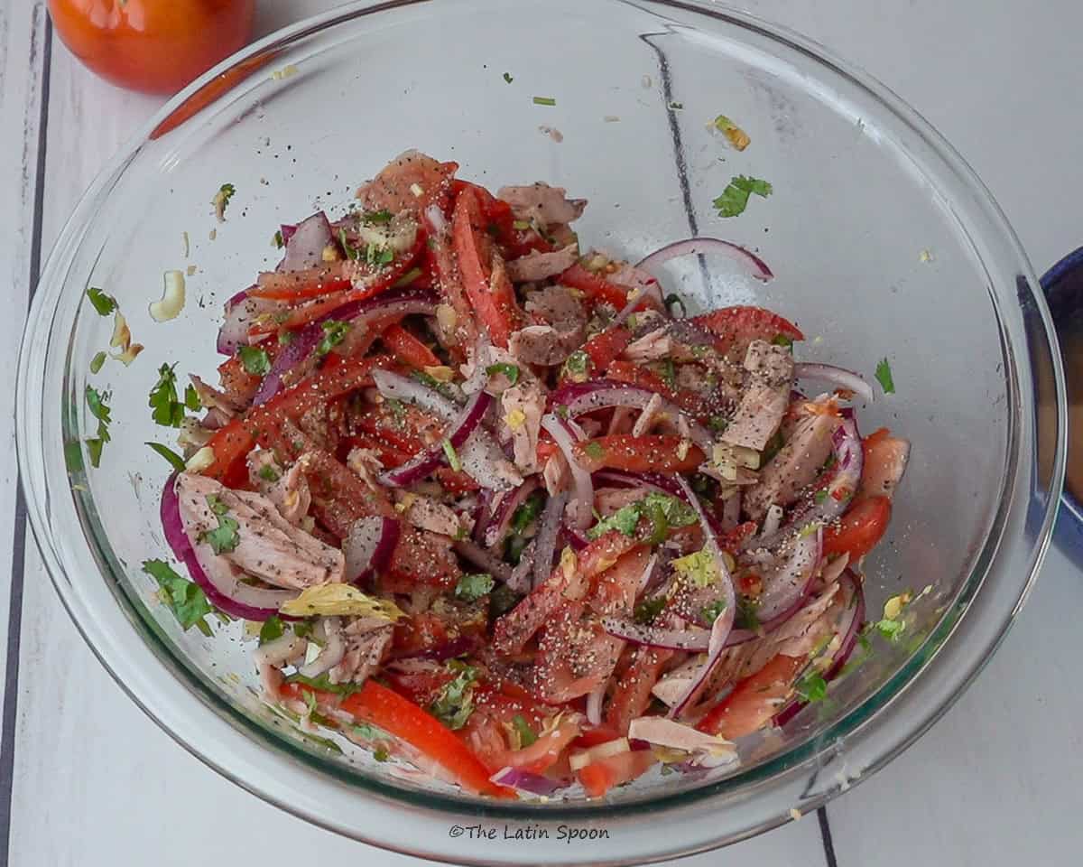 A glass bowl holding the mixed tuna salad with freshly added black pepper on top.