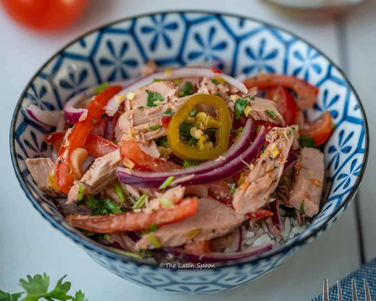 A round blue bowl showing the finished tuna salad with pieces of tomato and cilantro visible in the background.