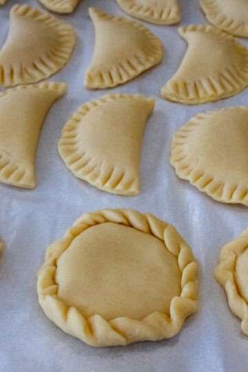 A tray of empanadas in different shapes is shown: some are round and others are half-moon shaped.
