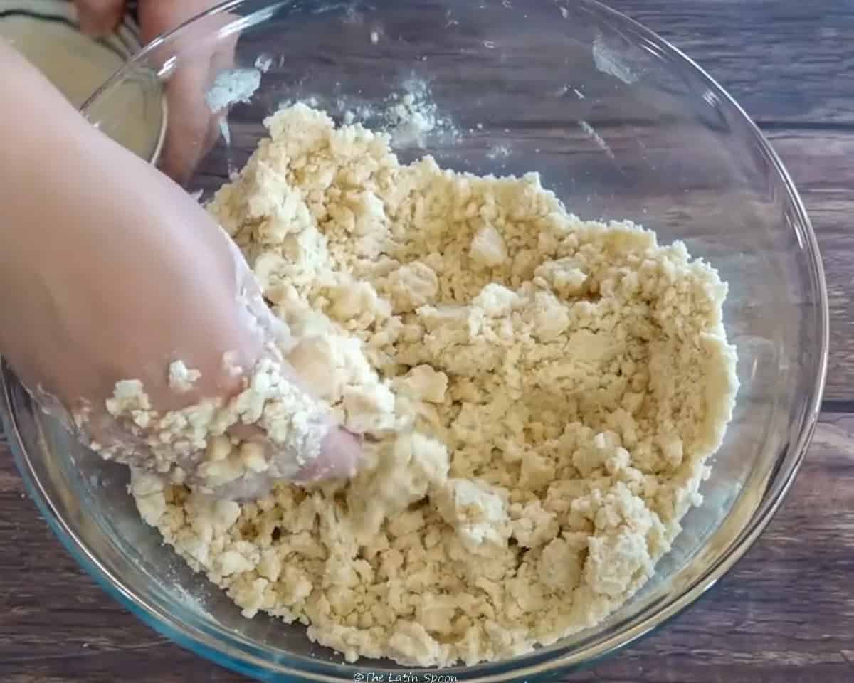 A bowl with a flour mixture being kneaded by hand is shown.
