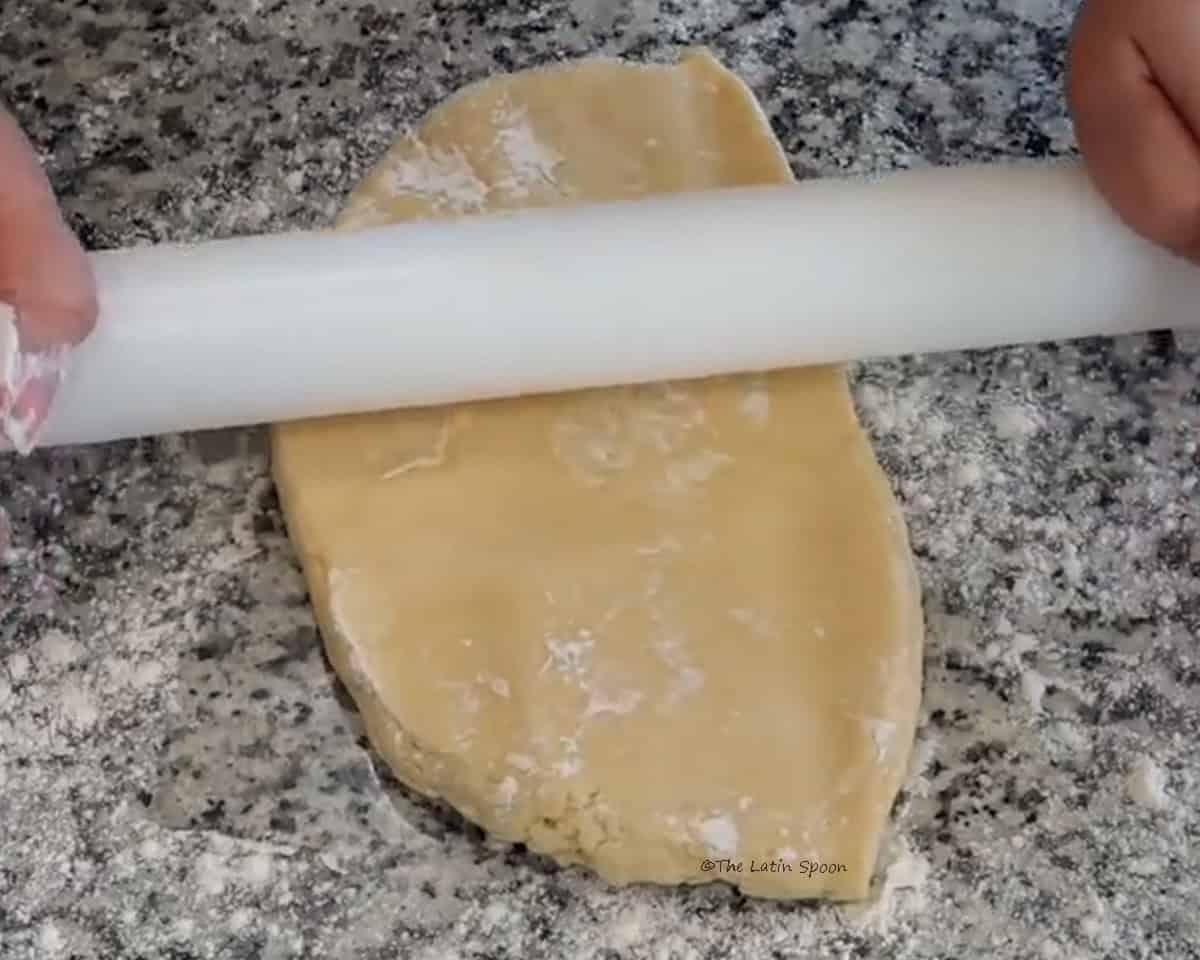 A ball of dough being rolled out with a rolling pin by two hands is shown.