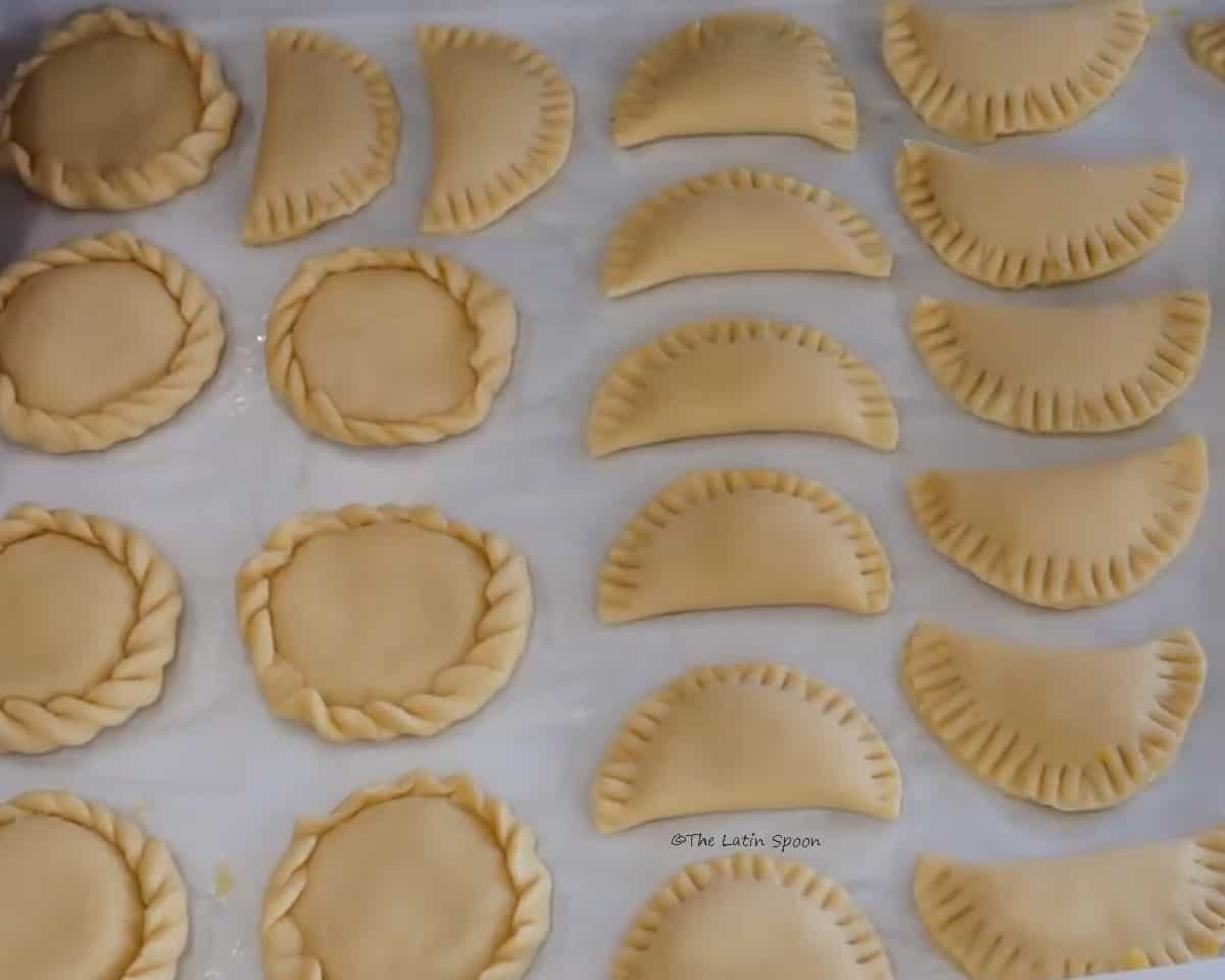 A tray of empanadas in different shapes is shown: some are round and others are half-moon shaped.