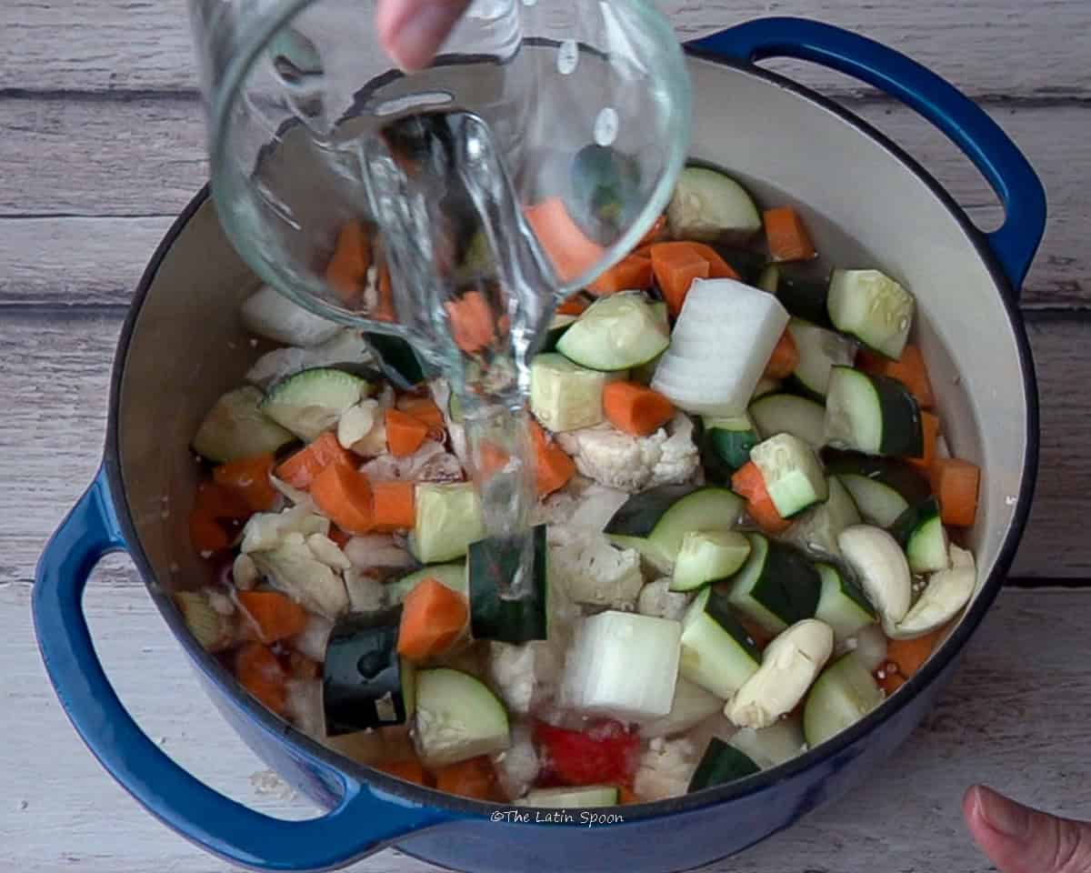 A pot with diced vegetables while a cup pours in water.