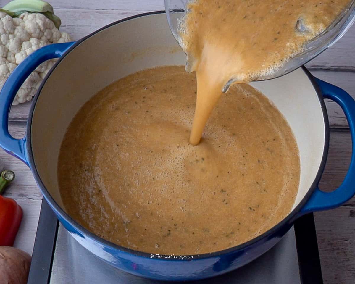 A pot on the stovetop while the blender pitcher pours in the blended vegetable mixture.