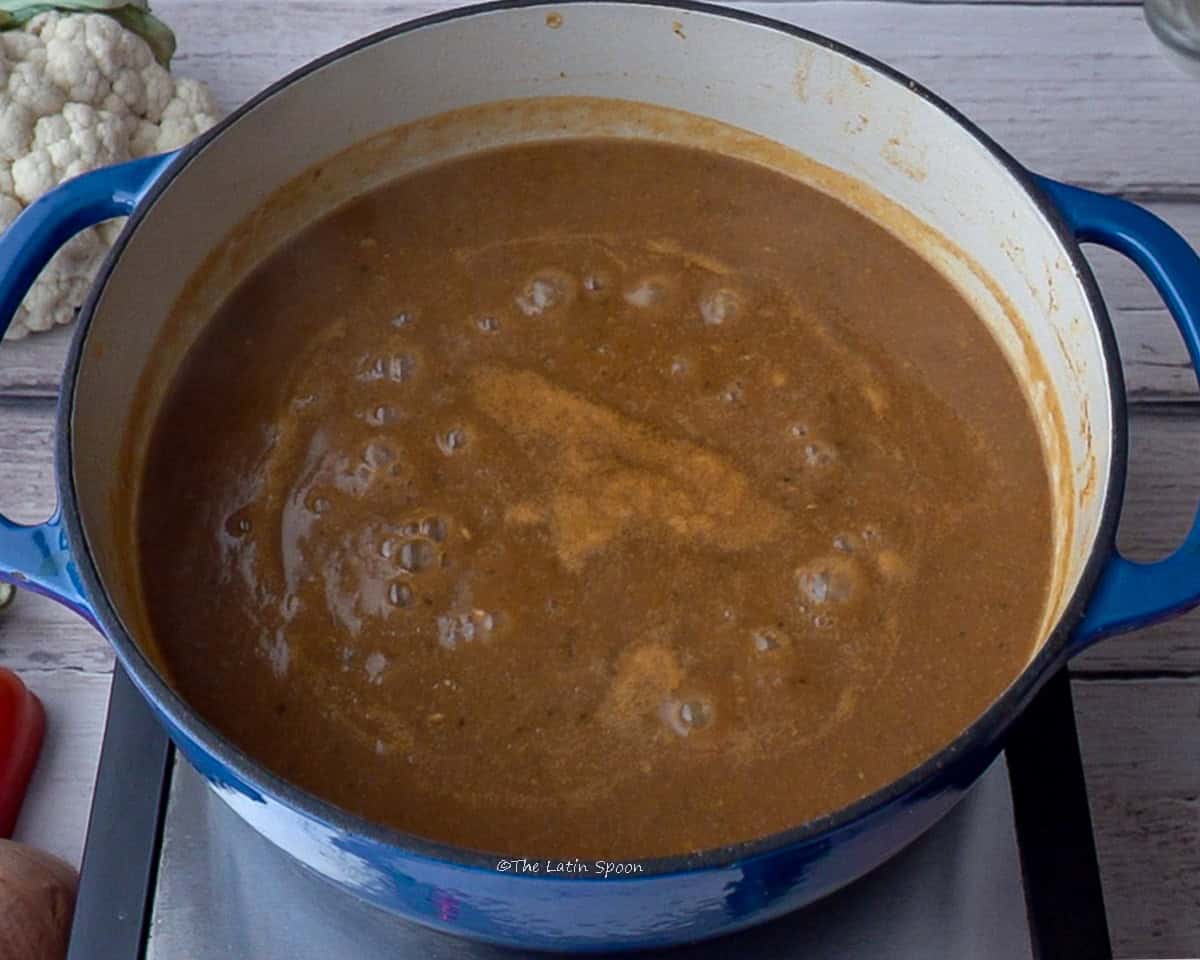 A pot on the stovetop with the liquid mixture inside and a cauliflower in the background.