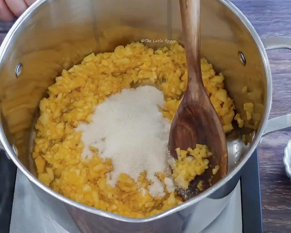 An aluminum bowl containing pineapple finely diced into small cubes and white sugar.