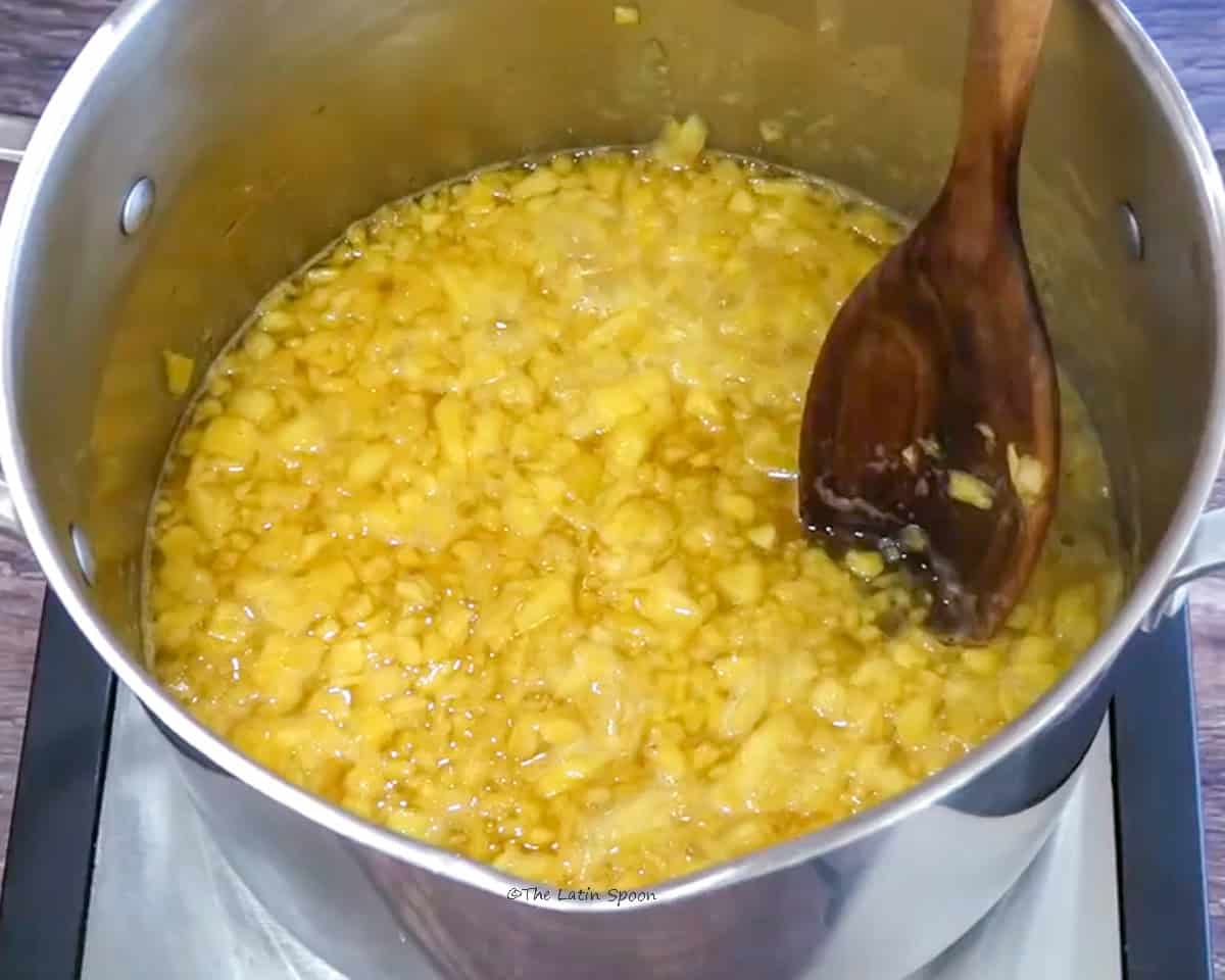 A deep pot containing chopped pineapple with water added, and a wooden spoon.