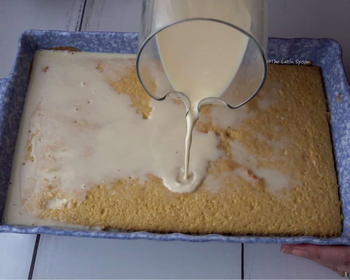The baking dish with the baked cake, while a pitcher pours the milk mixture over the top.