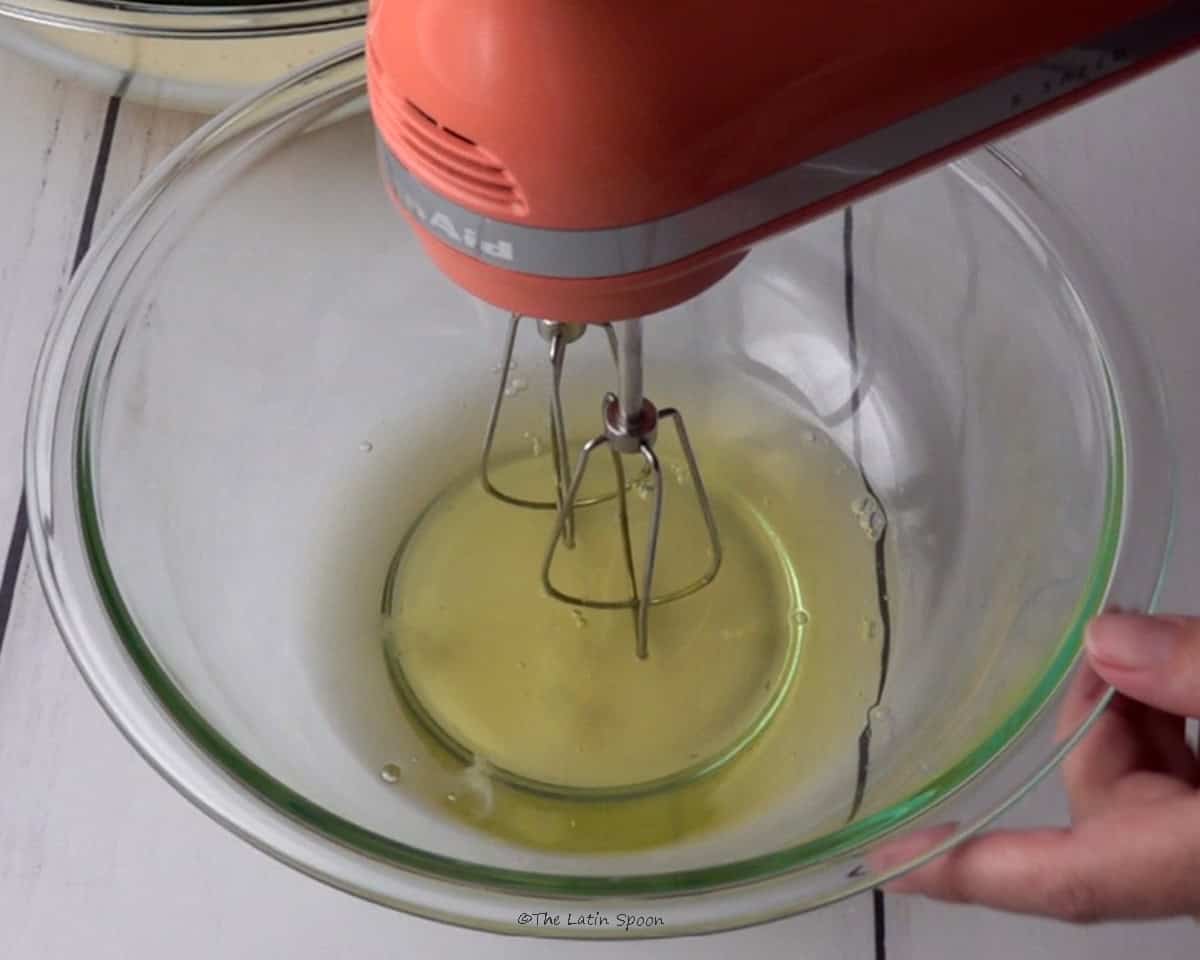 A bowl containing the egg whites, with an electric hand mixer placed inside.